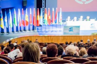 People sitting in lecture theatre with multiple country flags on stage