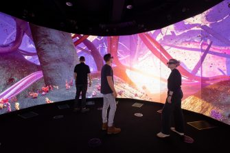 Photo of cylindrical screen with colourful projections and three people wearing 3D glasses standing in front