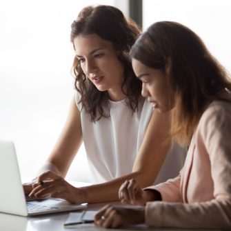 businesswomen workers talk discuss online project work together look at laptop in office, mentor teach intern, executive train employee using computer software