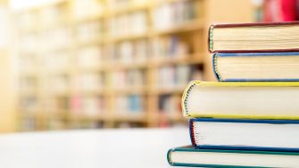 Stack and pile of books on table in public or school library.