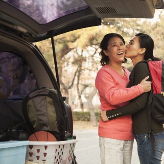 Mother and daughter embracing behind car on college campus