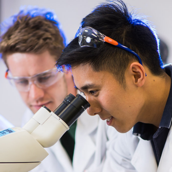 Three students one looking through a microscope