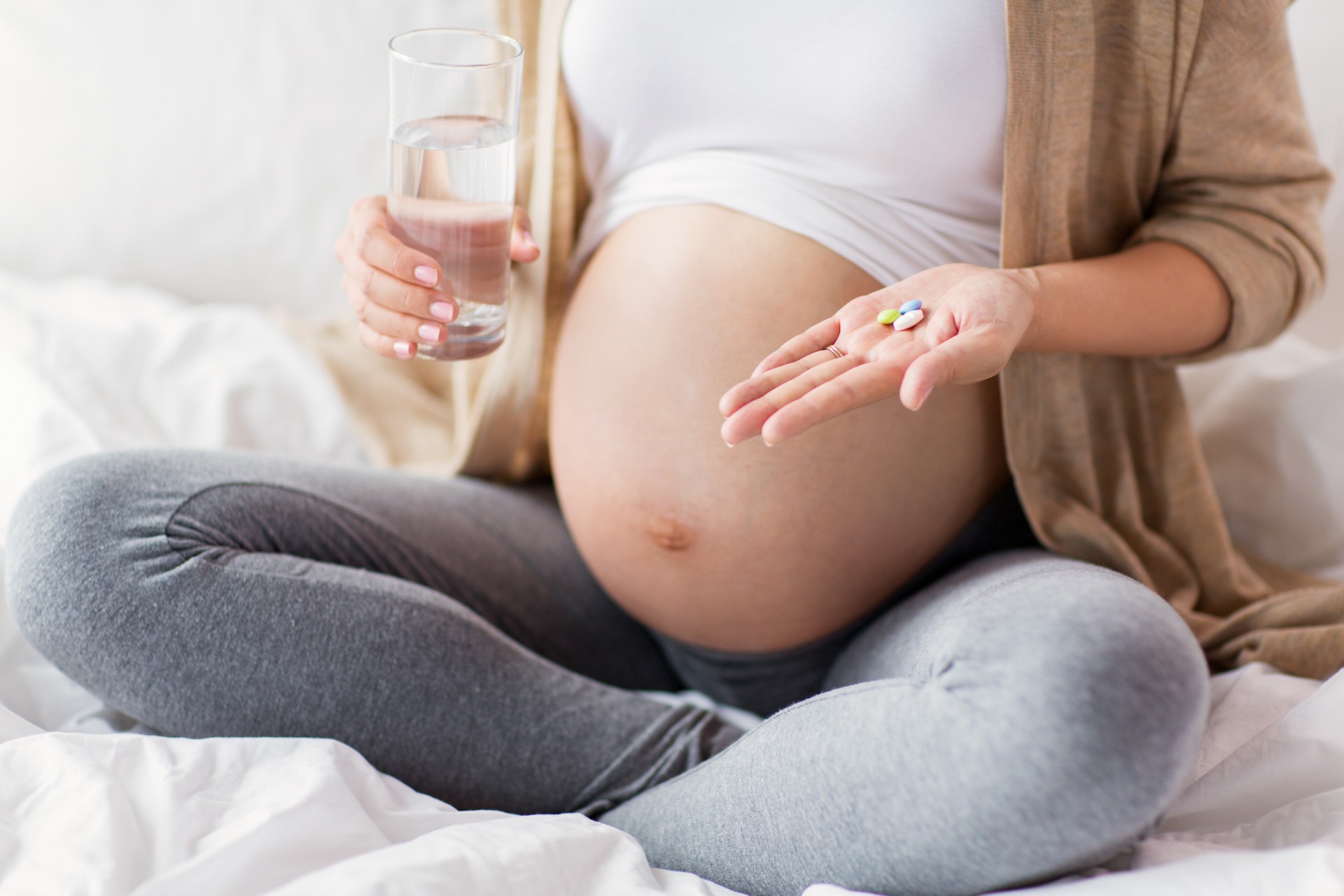 Close up of pregnant person sitting in bed at home with pills and glass of water