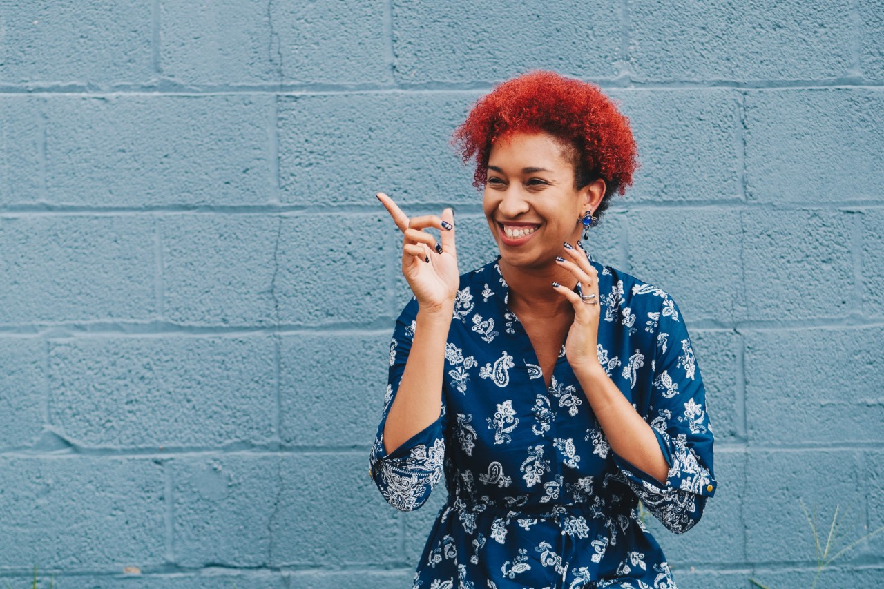 Woman with red hair smiling and pointing in front of a blue wall