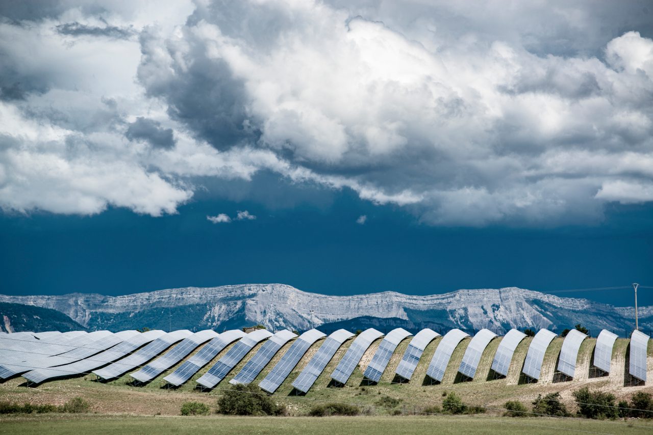 Big solar power plant with mountain ridge and dramatic clouds. Concept of environment protection and renewable energy generation to prevent climate change.