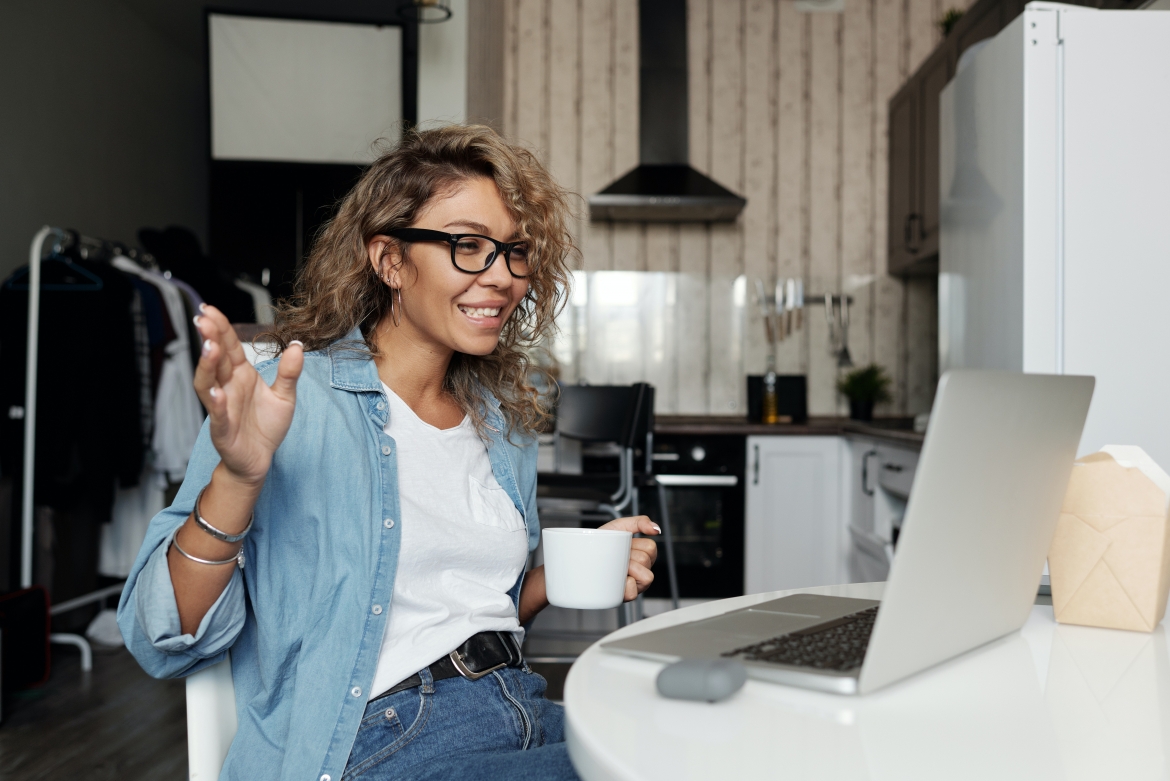 A woman engaged in a teleconference on her laptop with a mug in hand