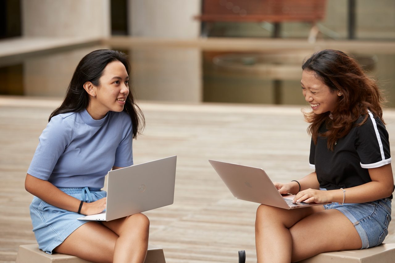 Students sitting and standing with laptops at outdoor courtyard