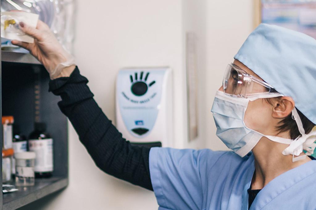 Lady in profile wearing hat and scrubs reaching to bookshelf